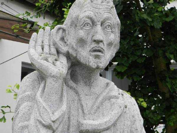 Bild: eine Steinstatur hält die Hand hinter das Ohr, so als ob sie intensiv zuhören würde. Wie in einer Seelsorgesituation.