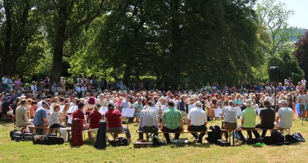 Quelle: Ulrike Müller Bild: In der Lichtentaler Allee findet der Gottesdienst der ACK am Pfingstmontag mit ca. 500 Personen statt. Sie sitzen unter blauem Himmel im Kreis um den Altar.