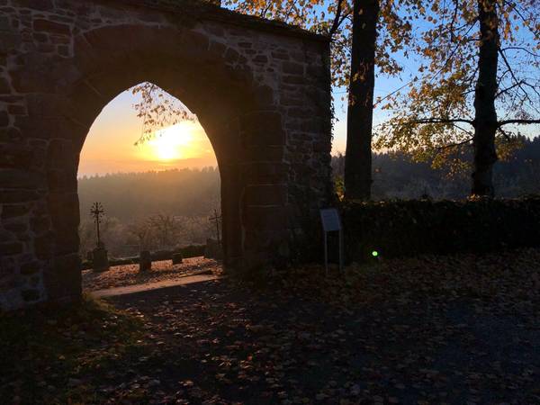 Bild: Hinter einem offenen Tor ist der Sonnenuntergang zu sehen, Symbol für Beerdigung und Hoffnung über den Tod hinaus.